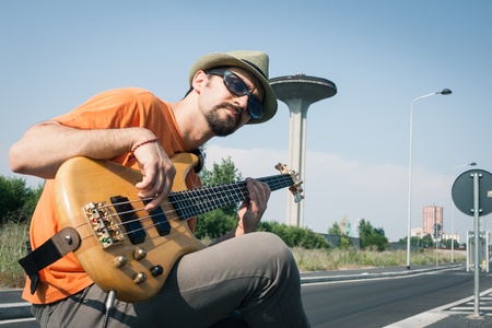 Young musician playing bass guitar in the middle of a suburban streetの写真素材