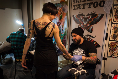 MILAN, ITALY - FEBRUARY 8: Tattoer looks at his work on a girl at Milano Tattoo Convention, international event dedicated to the world of tattoos, body piercing and body painting on FEBRUARY 8, 2014 in Milan.のeditorial素材