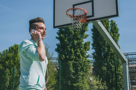Short hair girl with hoodie talking on phone in a basketball playgroundの写真素材
