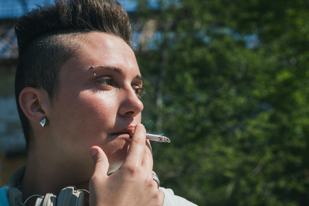 Portrait of short hair girl with hoodie smoking a cigaretteの写真素材