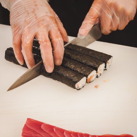 Detail of hands cutting sushi rolls with knifeの写真素材