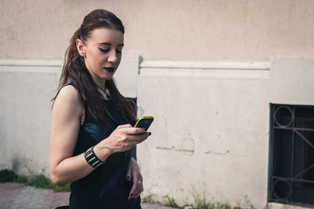 Pretty dark goth girl using phone in a city parkの写真素材
