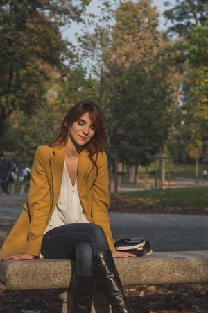 Redhead girl with yellow coat posing in a city parkの写真素材