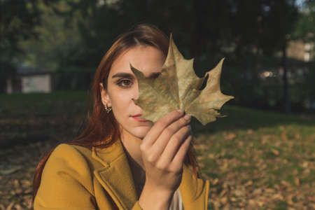 Redhead girl with yellow coat posing in a city parkの写真素材