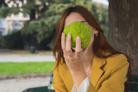 Redhead girl with yellow coat holding a fruit in her hand