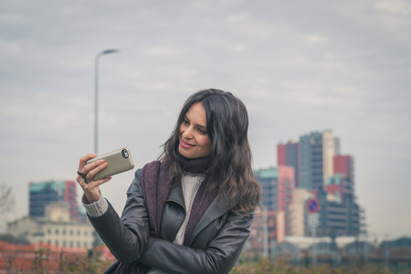 Beautiful young brunette with long hair taking a selfie in the city streetsの写真素材