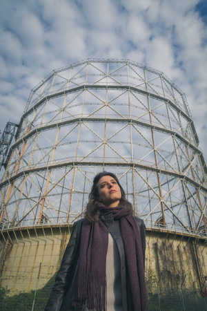 Beautiful young brunette with long hair posing in front of a gasometerの写真素材