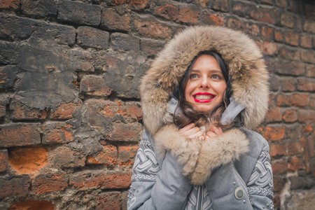 Beautiful young brunette with furry hood posing in the city streets
