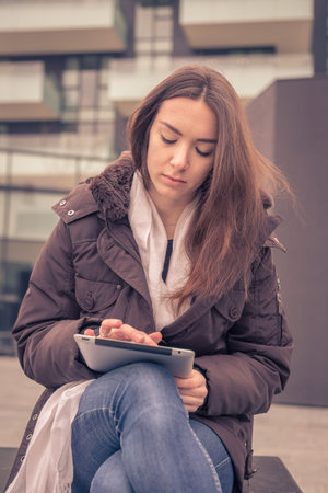 Young beautiful girl working with her tablet in the city streets