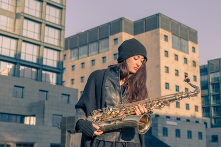 Beautiful young woman posing in the city streets with her saxophoneの写真素材
