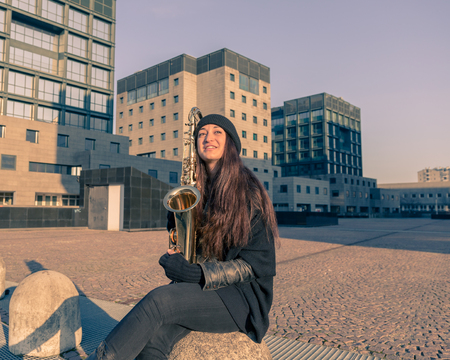 Beautiful young woman posing in the city streets with her saxophoneの写真素材