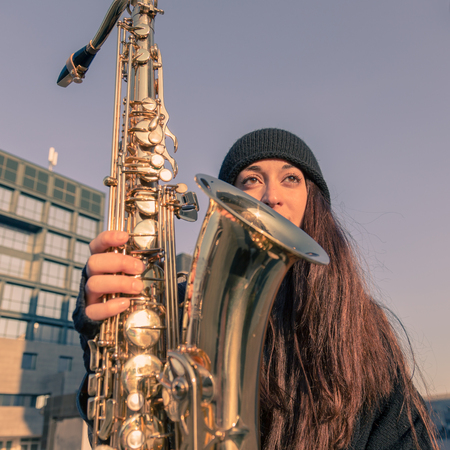 Beautiful young woman posing in the city streets with her saxophoneの写真素材
