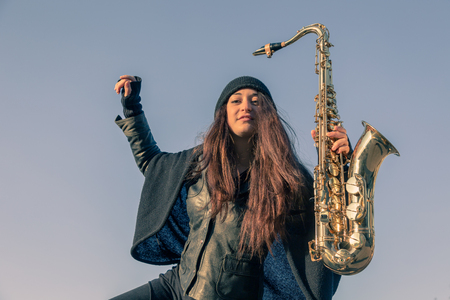 Beautiful young woman posing in the city streets with her saxophoneの写真素材