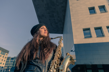Beautiful young woman posing in the city streets with her saxophoneの写真素材