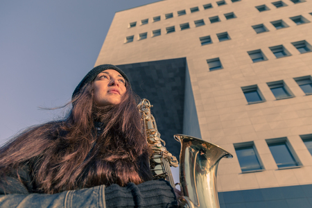 Beautiful young woman posing in the city streets with her saxophoneの写真素材