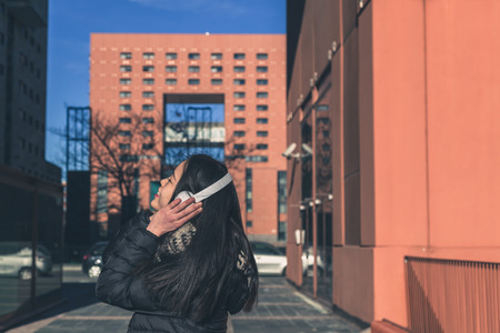 Young beautiful Chinese girl with headphones listening to music in the city streetsの写真素材