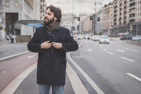 Young handsome bearded man with coat posing in the city streetsの写真素材