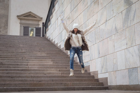 Beautiful young woman wearing ecological fur jumps down stairs - Concept of happiness, joy, freedom...