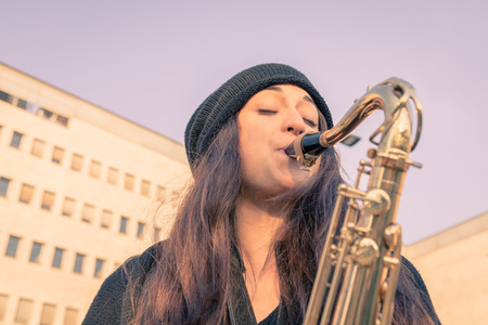 Beautiful young woman playing tenor saxophone in the city streetsの写真素材