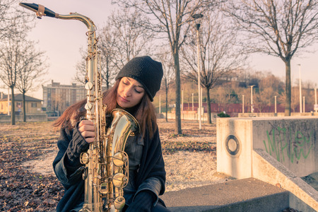 Beautiful young woman posing in the city streets with her saxophoneの写真素材