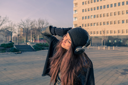 Beautiful young woman with headphones listening to music in the city streetsの写真素材