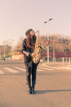 Beautiful young woman playing tenor saxophone in the city streetsの写真素材