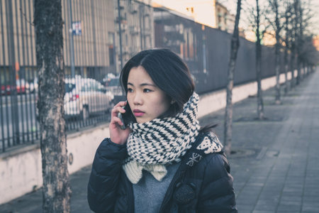 Young beautiful Chinese girl with long hair talking on phone in the city streets