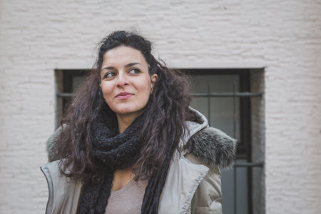 Beautiful young brunette with long curly hair posing in the city streets