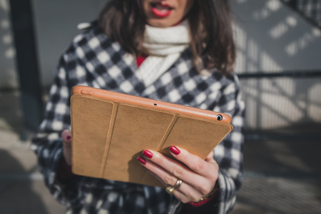 Detail of a young woman with long hair using her tablet in the city streetsの写真素材