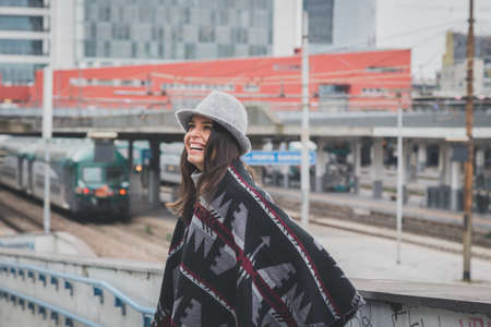 Beautiful young brunette with hat posing in the city streetsの写真素材