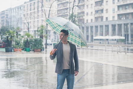Young handsome man with umbrella posing in the rainの写真素材