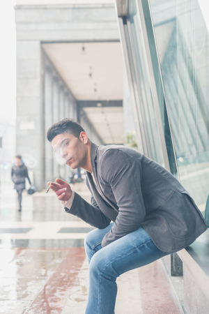 Young handsome man with short hair smoking a cigarette in the city streetsの写真素材