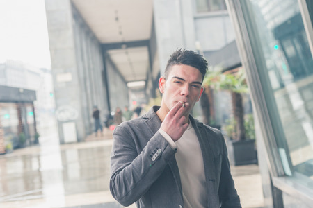 Young handsome man with short hair smoking a cigarette in the city streetsの写真素材