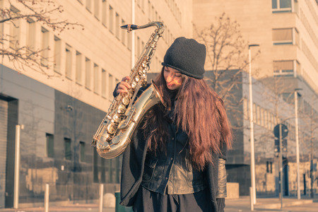 Beautiful young woman posing in the city streets with her saxophoneの写真素材