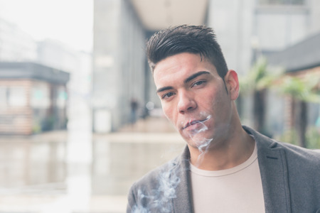 Young handsome man with short hair smoking a cigarette in the city streetsの写真素材