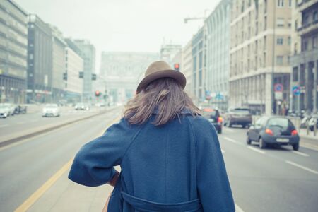 Beautiful young brunette with hat posing in the city streetsの写真素材