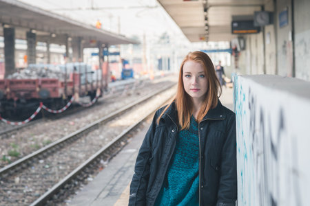 Beautiful young redhead girl posing in a railroad station