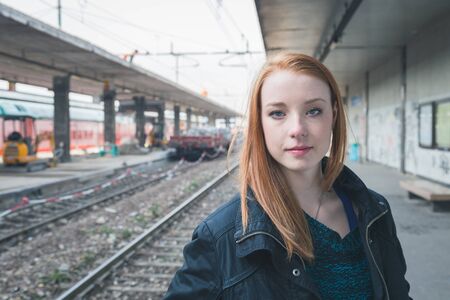 Beautiful young redhead girl posing in a railroad stationの写真素材