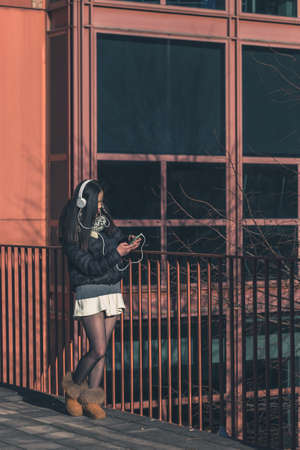 Young beautiful Chinese girl with headphones listening to music in the city streetsの写真素材