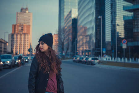 Beautiful Middle Eastern girl with long hair posing in an urban context at duskの写真素材