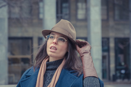 Beautiful young brunette with hat posing in the city streets