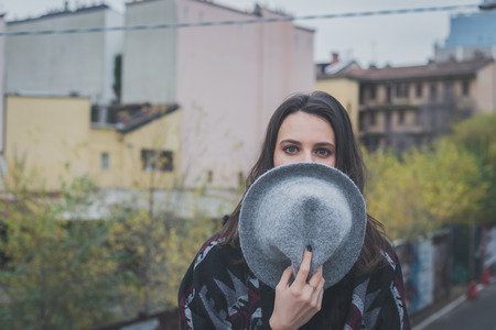 Beautiful young brunette with hat posing in the city streetsの写真素材