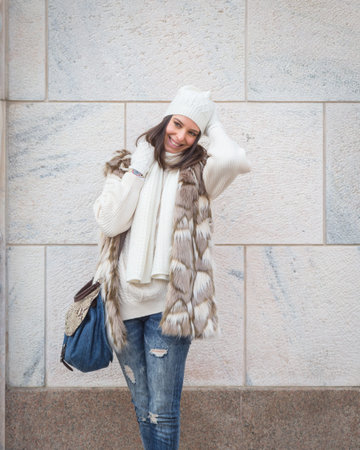 Beautiful young woman wearing ecological fur poses in the city streets