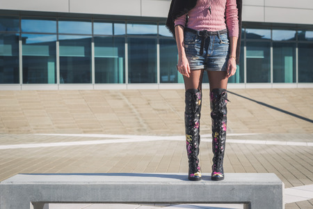 Detail of a beautiful young woman with over the knee boots standing on a benchの写真素材