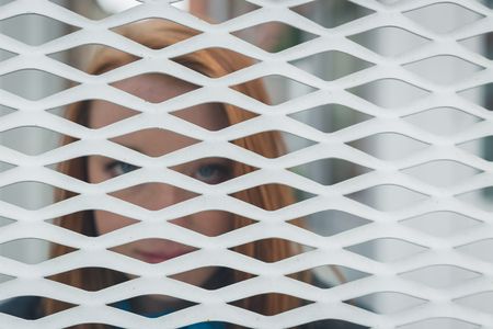 Beautiful young redhead girl posing behind a grate. Intentionally out of focus.の写真素材