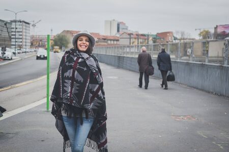 Beautiful young brunette with hat posing in the city streetsの写真素材