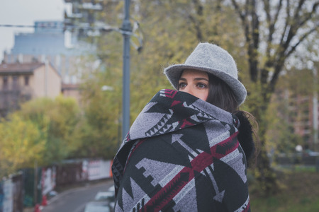 Beautiful young brunette with hat posing in the city streetsの写真素材