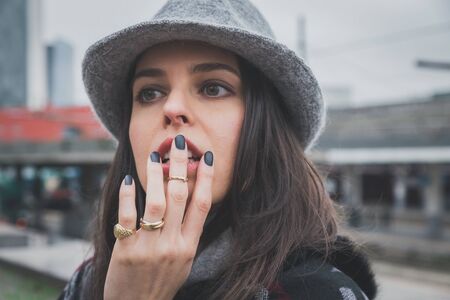 Beautiful young brunette with hat posing in the city streetsの写真素材