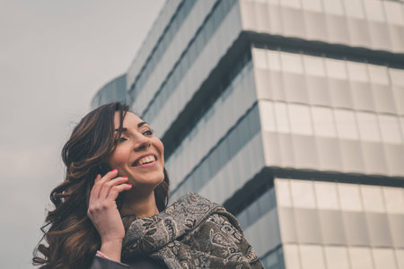 Beautiful young brunette with long hair talking on phone in an urban contextの写真素材