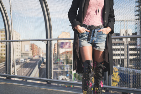 Detail of a beautiful young brunette with over the knee boots posing on a bridgeの写真素材